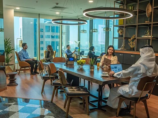  A dynamic shared workspace at Sahab Tower, Kuwait, where professionals collaborate and work individually in a bright, modern setting with large windows offering city views.
