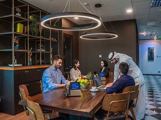 A dynamic shared workspace at Sahab Tower, Kuwait, where professionals collaborate and work individually in a bright, modern setting with large windows offering city views.